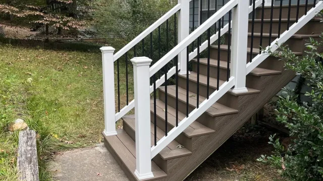 Outdoor staircase with brown steps and white railings leading to a blue house with red shutters.