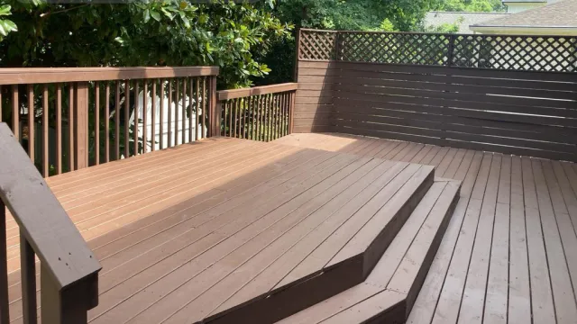 Clean wooden backyard deck with railing, steps, and privacy fence under natural daylight.