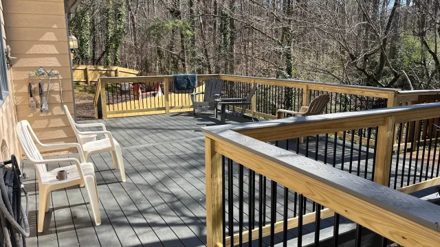 Spacious wooden deck with beige chairs and railing overlooking a wooded backyard on a sunny day
