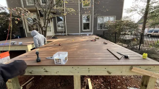 Construction workers building a wooden deck attached to a house on a clear day with tools scattered on the deck.