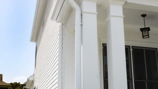 White house exterior with columns, siding, black framed windows, and a hanging lantern light under the porch roof.