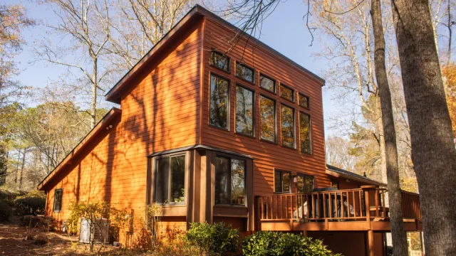 Modern two-story house with grey siding, multiple windows, wooden deck, and outdoor grill area on a sunny day.