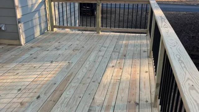 Newly built wooden deck with light natural wood planks and black metal railing in suburban backyard.