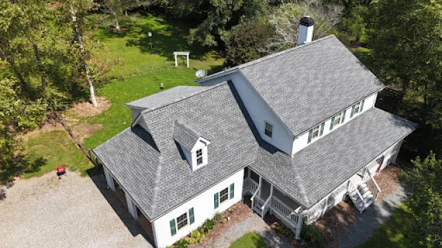 Aerial view of a large white two-story house with gray roof surrounded by green trees and lawn.