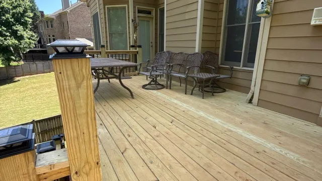 Spacious wooden deck attached to a beige house with outdoor metal furniture and solar post lights under a clear sky.