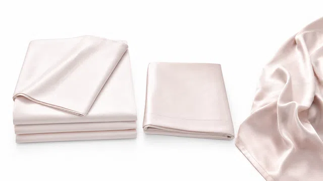 Soft pink satin bed sheets and pillowcases folded neatly with a satin fabric draped beside them.