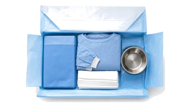 Surgical kit with blue sterile gown, folded drape, white towels, and metal bowl in opened blue packaging.