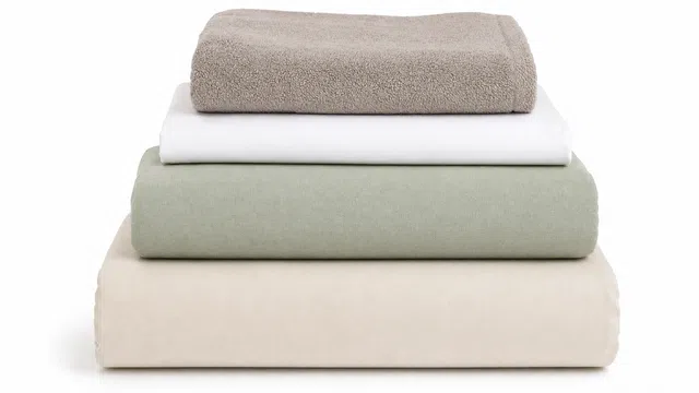 Stack of folded towels and bed linens in beige, white, and light green against a white background