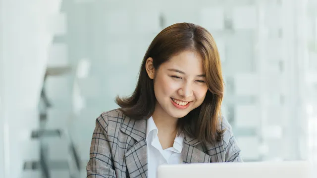 Young woman smiling while working on a laptop in a modern office environment.
