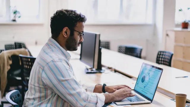 Professional man working on a laptop in a modern office environment with natural light.