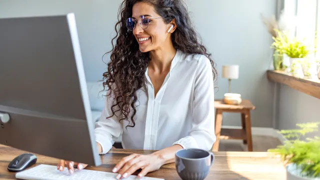 Smiling woman with curly hair using a desktop computer in a bright, modern office space.