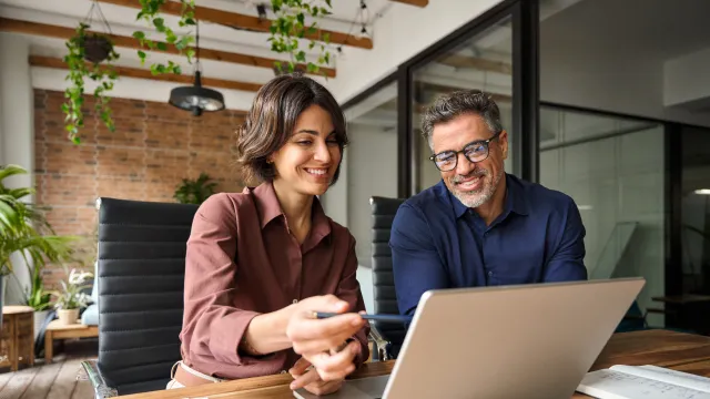Two professionals discussing a project while working on a laptop in a modern office setting.