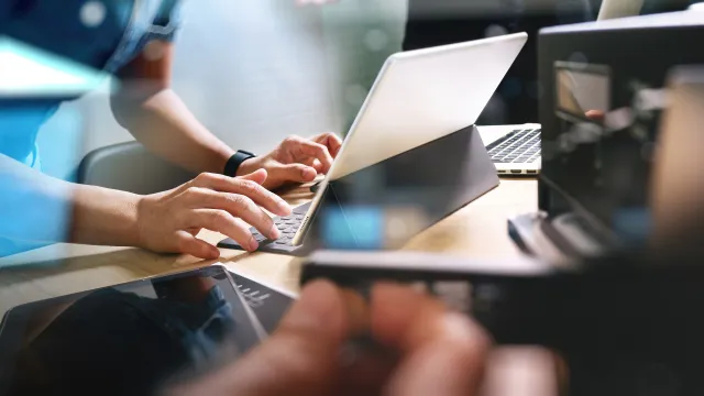 A person typing on a laptop surrounded by modern technology and office elements.