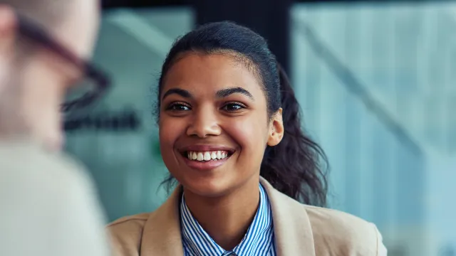 Smiling woman in professional attire engaging in conversation during a meeting with a laptop nearby.