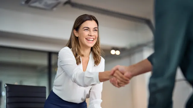 Businesswoman smiling and shaking hands in a modern office setting.