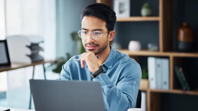 Concentrated man in glasses working on a laptop in a modern office setting.