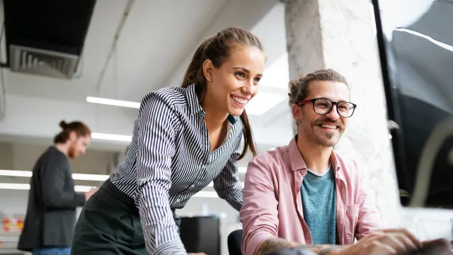 Two colleagues collaborate at a modern office workspace, smiling and engaging in discussion.