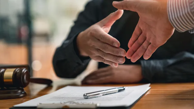 Two business professionals shaking hands over a contract on a wooden desk.