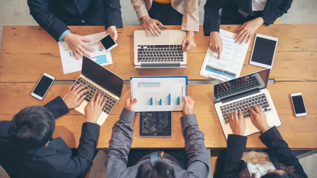 Aerial view of a business meeting with laptops, charts, and professionals collaborating on strategies.