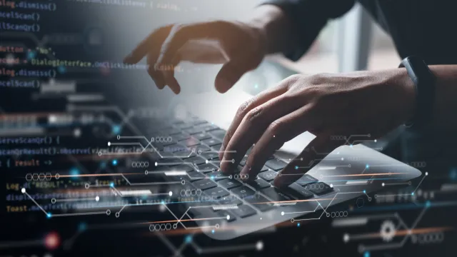 Close-up of hands typing on a laptop keyboard with code and digital graphics overlay.
