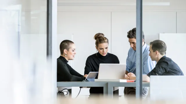 Four professionals collaborating around a laptop in a modern office environment.