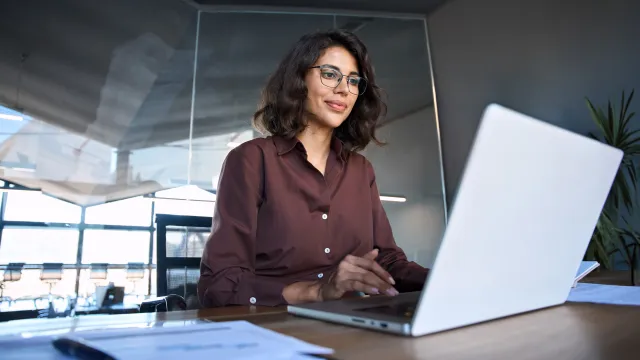 Two professionals discussing documents in a modern office setting with a laptop.