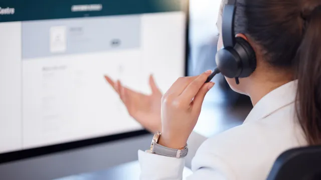 Woman in headset interacting with computer screen in a customer service setting.