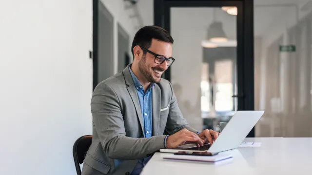 Smiling businessman working on a laptop in a modern office setting.