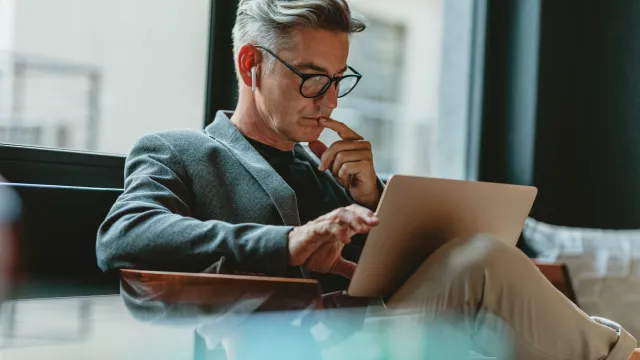 Man working on a laptop while sitting in a modern office environment, deep in thought.