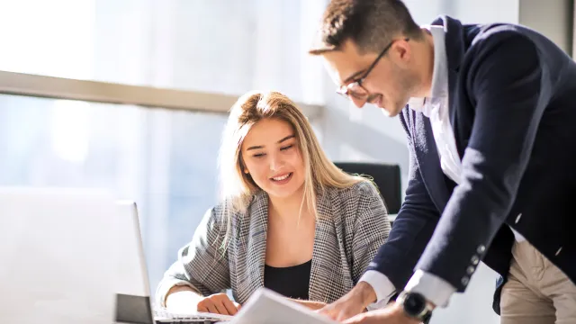 Professionals collaborating at a desk with a laptop and documents in a bright office environment.
