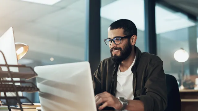 Smiling man working on a laptop in a modern office environment.