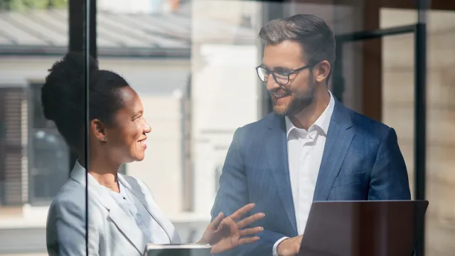 Professionals discussing ideas in a modern office, with a laptop and notebook in hand.