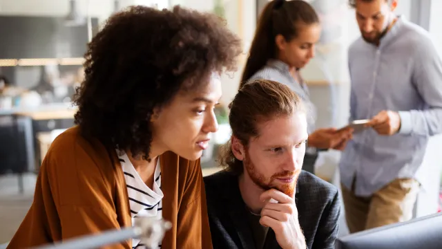 A diverse team collaborates in a modern office setting, focused on a computer screen.