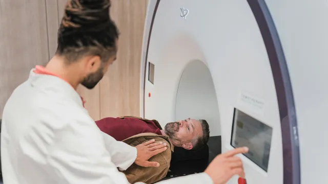 Radiologist preparing middle-aged man for MRI scan inside modern medical imaging machine.