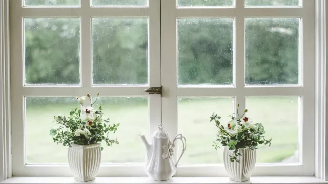 a couple of white vases with flowers in them by a window