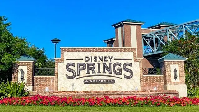 Disney Springs welcome sign surrounded by flowers and greenery under a clear blue sky.