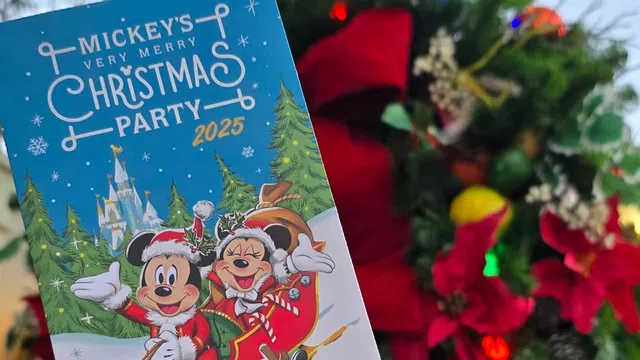 Hand holding a Mickey's Very Merry Christmas Party 2025 Magic Kingdom ticket with holiday decorations in the background