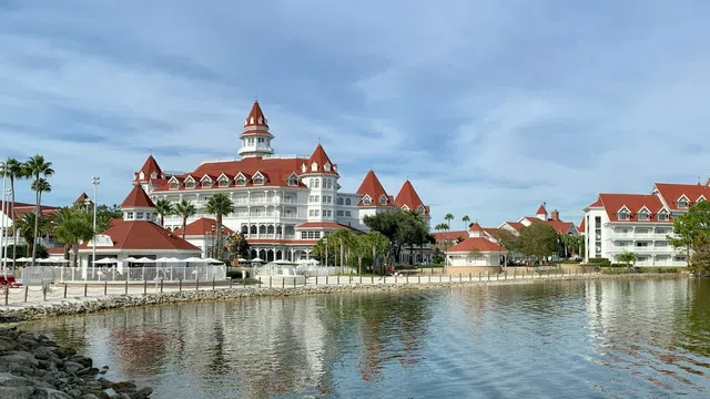 Disney's Grand Floridian Resort & Spa - a waterfront resort with red roofs, white buildings, palm trees, and calm reflective water under a blue sky.