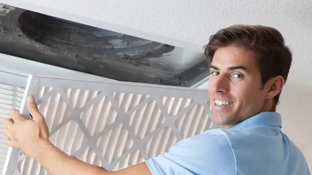 Man in blue shirt installing or replacing an air filter in a ceiling vent with a smile.