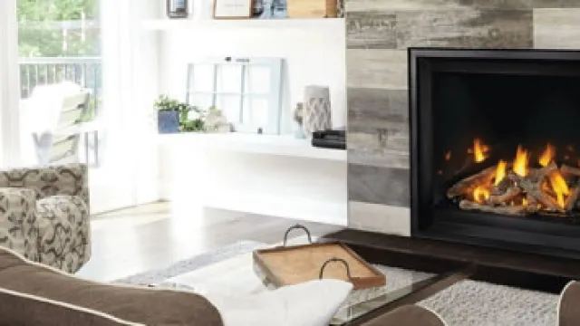 Cozy living room with a stone fireplace, glass coffee table, comfortable armchair, and natural light.