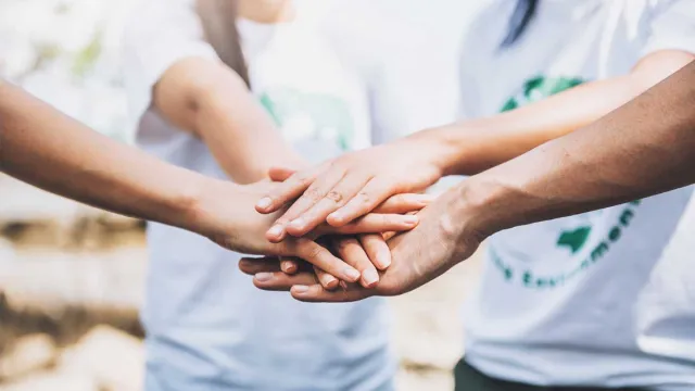Group of people stacking hands together showing unity and teamwork outdoors with white shirts