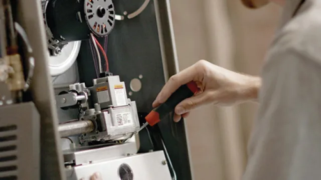 Technician repairing a furnace with a screwdriver, focusing on mechanical components inside the unit.