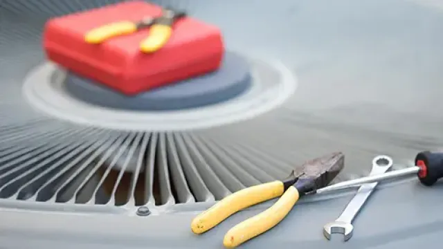 Yellow-handled pliers, wrench, and screwdriver on an air conditioner unit with a red toolbox in background.