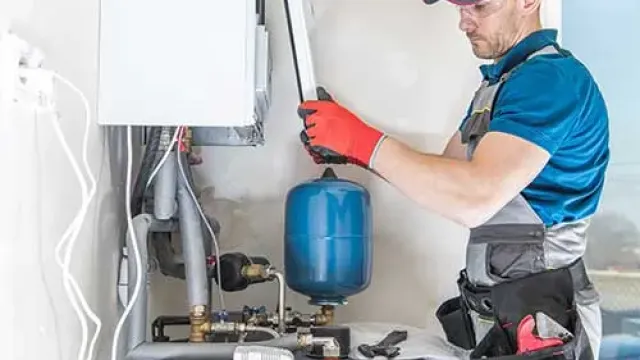 Technician in red gloves repairing or installing a boiler system with tools and a blue pressure tank.