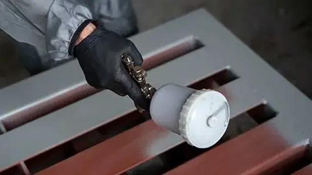 Worker in protective gloves spraying paint onto metal surface with spray gun indoors