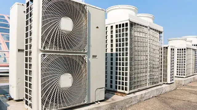 Row of large outdoor air conditioning units installed on a rooftop under clear blue sky.