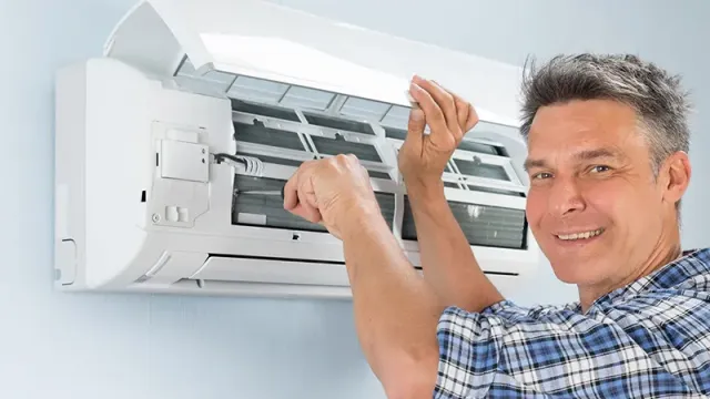 Technician wearing checkered shirt repairing and cleaning a wall-mounted air conditioner indoors.