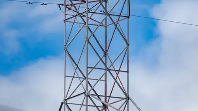 Close-up of an electrical transmission tower with power lines against a cloudy blue sky.