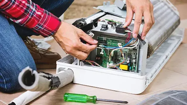 Technician repairing or assembling an air conditioner indoor unit, with tools and wires visible