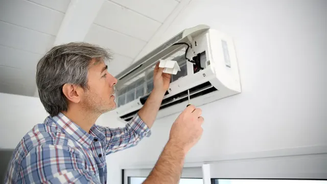 Man in plaid shirt repairing a wall-mounted air conditioning unit with a screwdriver indoors.